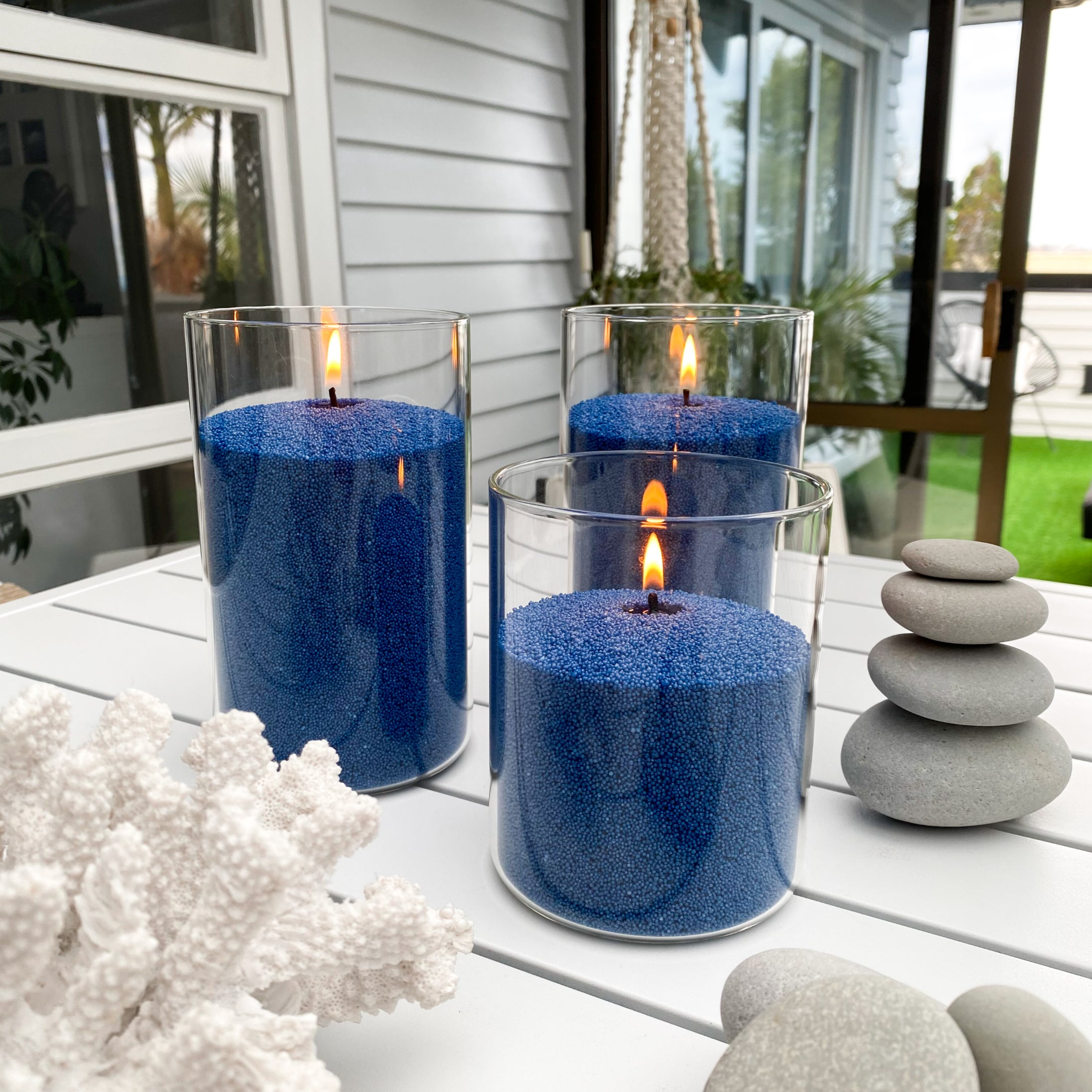 Blue sand wax candles in glass holders on a table with decorative stones and coral. Featuring a unique candle experience.