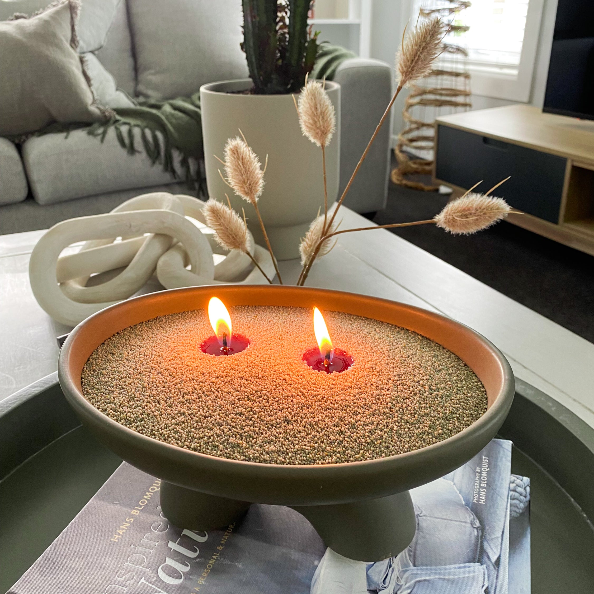 Decorative candle in a bowl with olive coloured sandwax on a table in a living room.