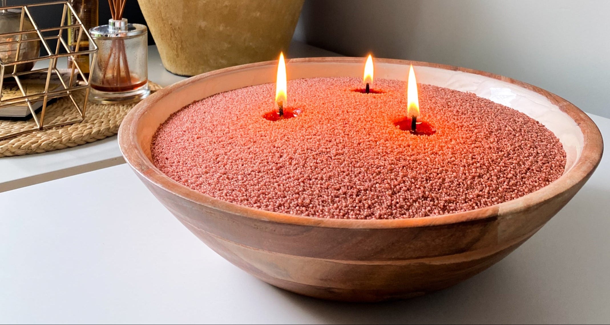 Large wooden bowl filled with rustic coral sand wax with three wicks. 