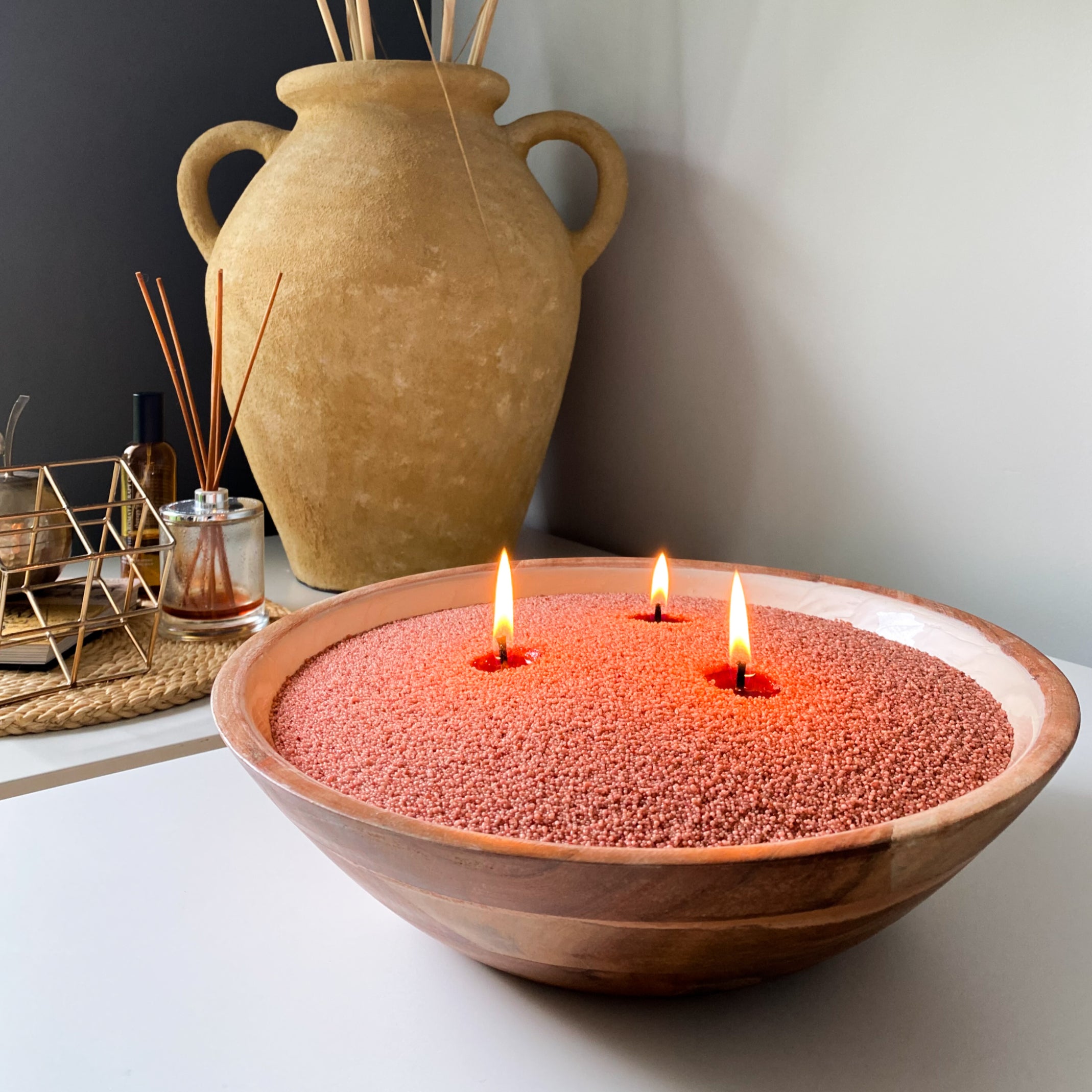 Large wooden bowl filled with rustic coral sand wax with three wicks. 